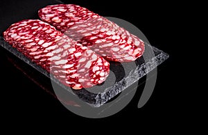 Sliced salami on a slate serving Board. Black isolated background