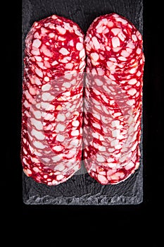 Sliced salami on slate serving Board. Black isolated background. Top view