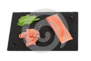 Sliced salmon fillet on the black shale board, with lemon and salad. On white background