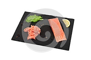 Sliced salmon fillet on the black shale board, with lemon and salad. On white background