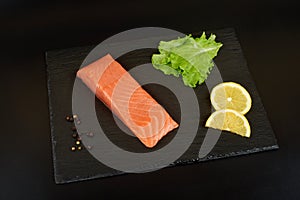 Sliced salmon fillet on the black slate table, with lemon and salad.