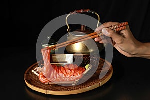 Sliced salmon fish Sashimi in the boat with the chopsticks in the hand on the black wooden table with Brass Teapots and tea cup in