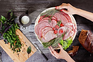 Sliced sausage, hands holding the dish, wooden countertop, chopped basil