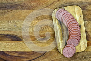 Sliced sausage on mini cutting board with wooden background