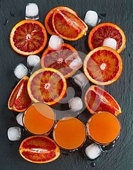 Sliced Sicilian red oranges and orange juice in small glasses on black stone background. Top view