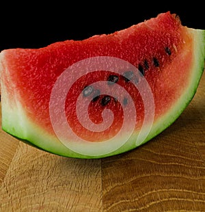 Sliced skib of ripe watermelon on a wooden board on a black background