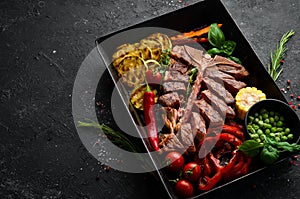 Sliced steak on the bone with grilled vegetables and spices. T-bone steak. Top view. Rustic style