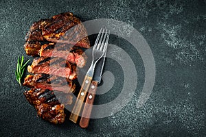 Sliced steak ribeye, grilled with pepper, garlic, salt and thyme on a dark stone background. Top view. Flat lay