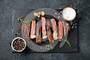 Sliced steak Striploin, grilled with pepper, garlic, salt and thyme served on a slate chopping Board on a dark stone background. T