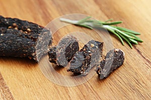 Sliced stick of biltong snack and rosemary seasoning on a wooden surface