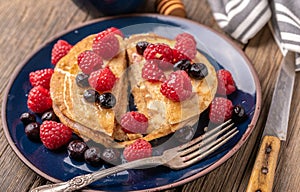 Sliced sweet homemade pancakes with raspberries and blueberries on blue plate