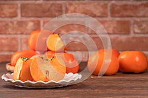 Sliced sweet persimmon kaki in a bamboo sieve basket on dark wooden table with red brick wall background, Chinese lunar new year