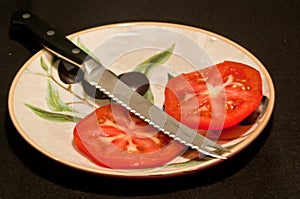 Sliced tomato a serrated knife blade with black handle on a round, ceramic painted print plate