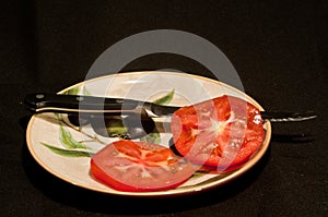 Sliced tomato a serrated knife blade with black handle on a round, ceramic painted print plate