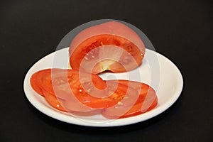 Sliced tomato slices on white plate isolated on black background