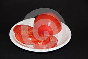 Sliced tomato slices on white plate isolated on black background