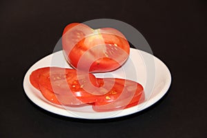 Sliced tomato slices on white plate isolated on black background