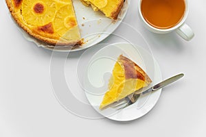Sliced upside down pineapple cake with cup of tea on white table. Summer tropical dessert. Top view. Copy space