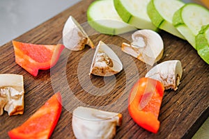 Sliced vegetables on a cutting wooden board: mushrooms, zucchini, red bell pepper