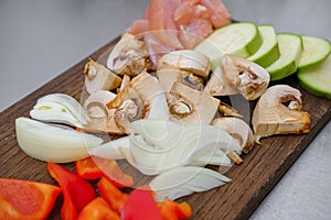 Sliced vegetables on a cutting wooden board: mushrooms, zucchini, red bell pepper