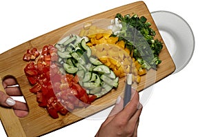 Sliced vegetables: tomato, cucumber, paprika, green onion, dill and parsley sprinkle from cutting board to glass bowl