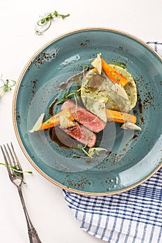 Sliced venison fillet steak with mashed potato and vegetables on blue plate
