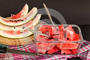 Sliced watermelon in glass container with black seeds on black background with watermelon peels