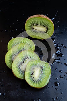 Sliced and whole kiwi fruit against a dark background, the vertical location of the photo