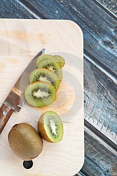 Sliced and whole kiwi fruit on a chopping Board and knife, wooden background