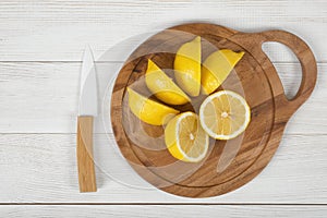 Sliced and whole lemons on cutting board with a knife next to it in top view