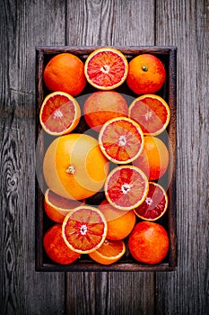 Sliced and whole ripe juicy blood oranges and grapefruit in the box on wooden background.