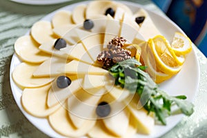 Sliced â€‹â€‹cheese on a white plate with nuts, olives and lemon