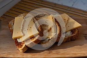 Sliced â€‹â€‹hard cheese sandwiches on bran bread on a wooden board, simple breakfast and healthy, quick snack