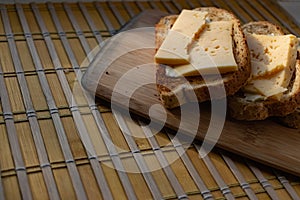 Sliced â€‹â€‹hard cheese sandwiches on bran bread on a wooden board, simple breakfast and healthy, quick snack