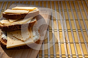 Sliced â€‹â€‹hard cheese sandwiches on bran bread on a wooden board, simple breakfast and healthy, quick snack