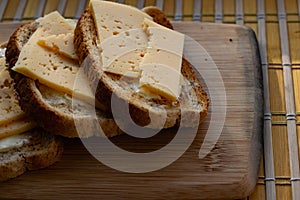 Sliced â€‹â€‹hard cheese sandwiches on bran bread on a wooden board, simple breakfast and healthy, quick snack