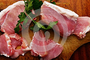 Sliced â€‹â€‹pieces of fresh raw meat and a branch of parsley on a cutting board.