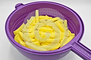 Sliced â€‹â€‹potatoes in purple plastic colander