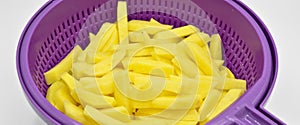 Sliced â€‹â€‹potatoes in purple plastic colander