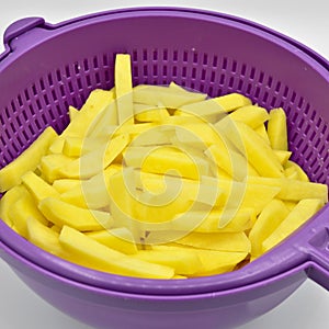 Sliced â€‹â€‹potatoes in purple plastic colander