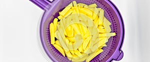 Sliced â€‹â€‹potatoes in purple plastic colander