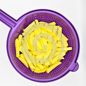 Sliced â€‹â€‹potatoes in purple plastic colander