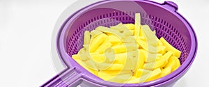 Sliced â€‹â€‹potatoes in purple plastic colander