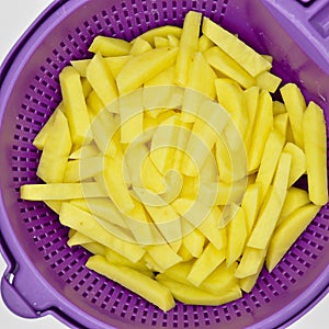 Sliced â€‹â€‹potatoes in purple plastic colander