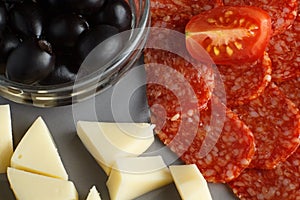 Sliced â€‹â€‹salami sausage, chir and olives on a gray background