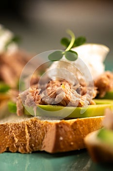 Slices of baguette with canned tuna, cheese and sliced avocado. dinner table, close-up.