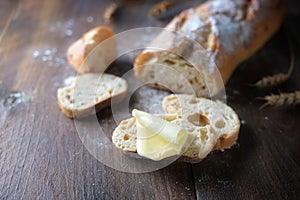 Slices from baguette or French bread with a piece of butter on dark rustic wood, copy space