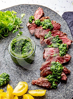 Slices of beef steak with chimmichuri sauce on gray stone plate