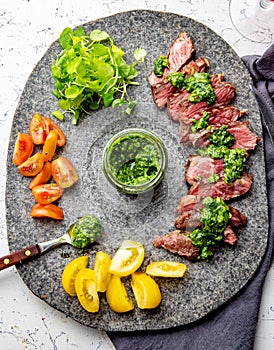 Slices of beef steak with chimmichuri sauce on gray stone plate