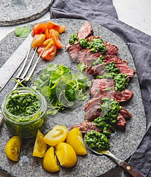 Slices of beef steak with chimmichuri sauce on gray stone plate